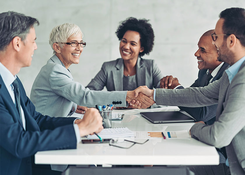 Business people smiling and shaking hands around conference table